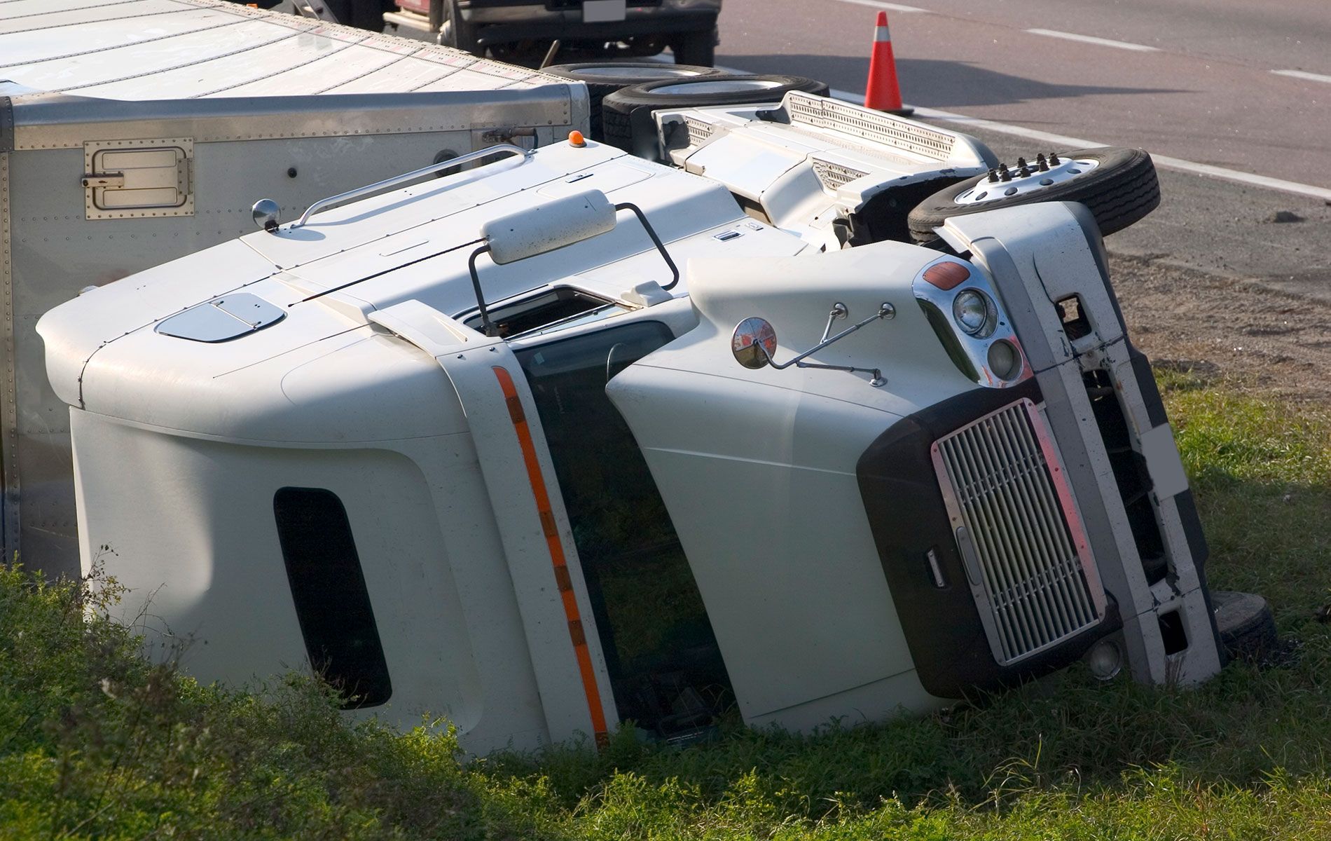 A white semi truck is turned over on its side on the side of the road.