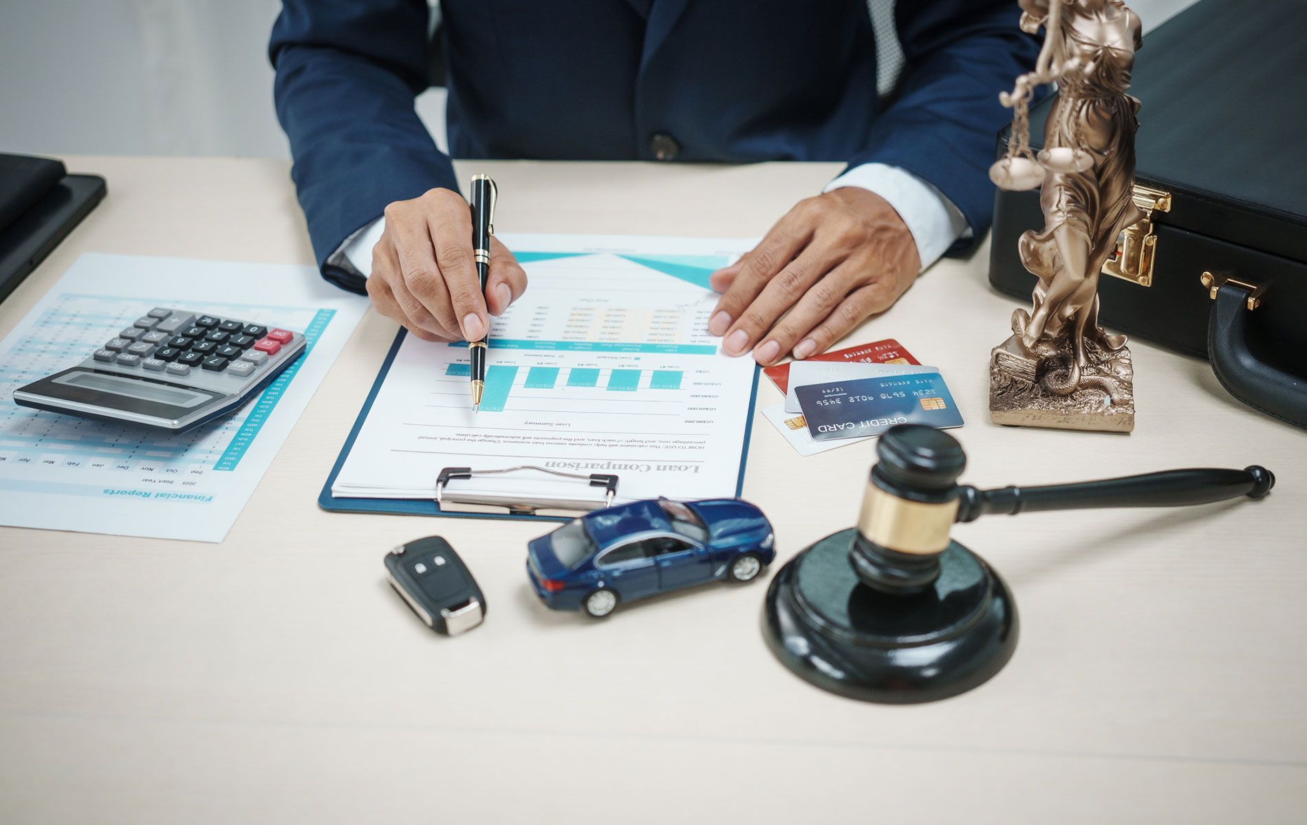 A man is sitting at a desk with a calculator , a car key , and a gavel.