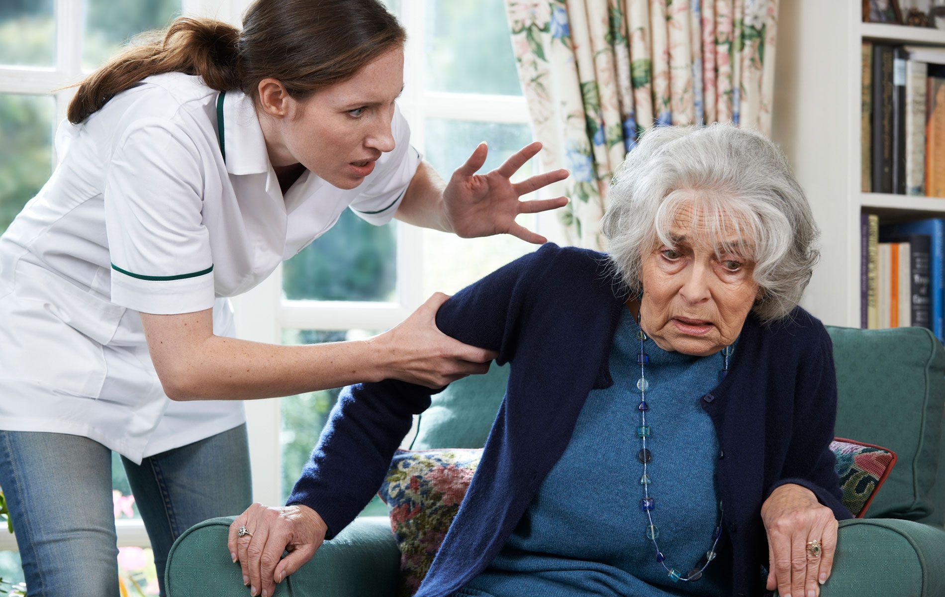 A nurse is helping an elderly woman sit on a couch.