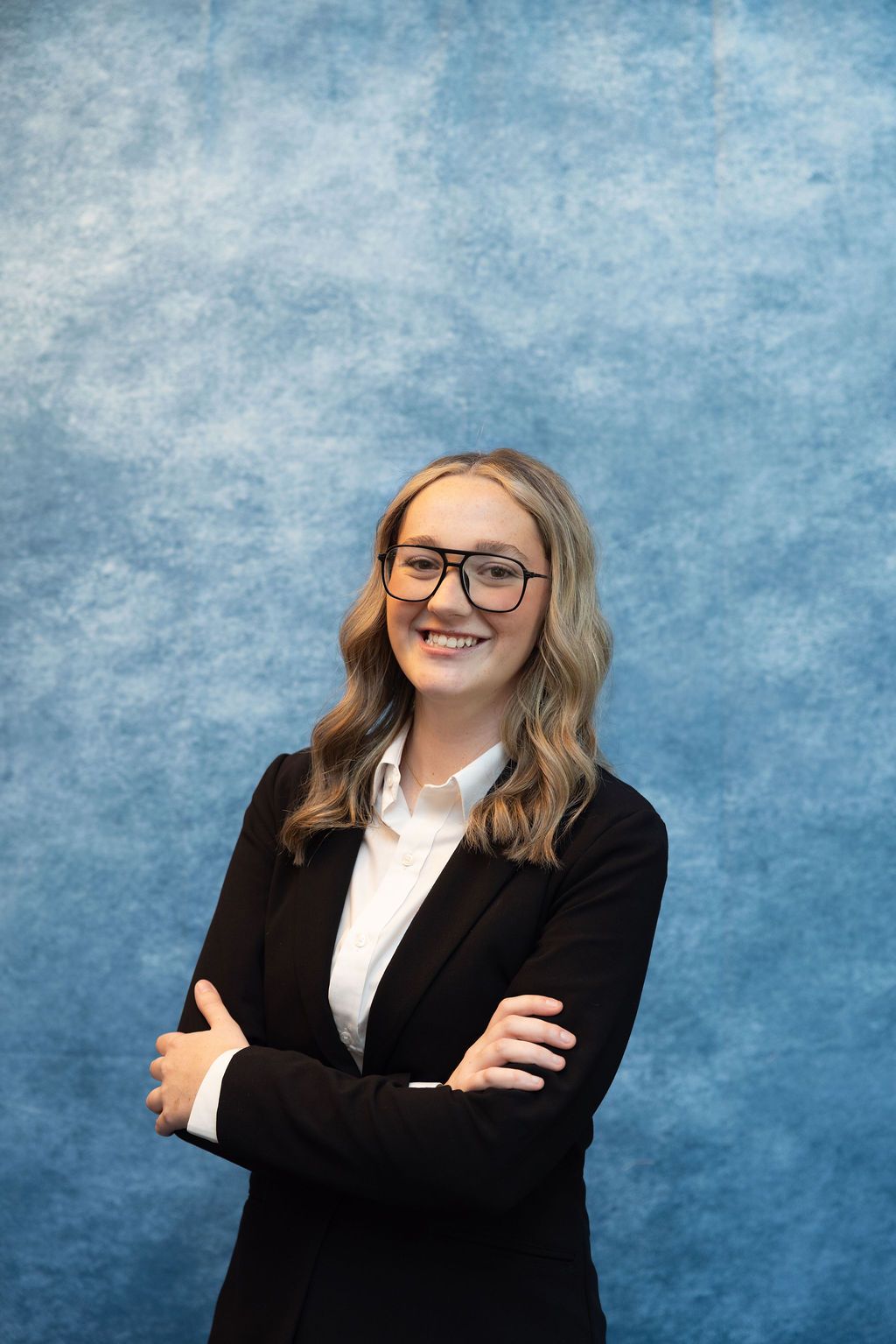 a woman wearing glasses and a white shirt is smiling for the camera .