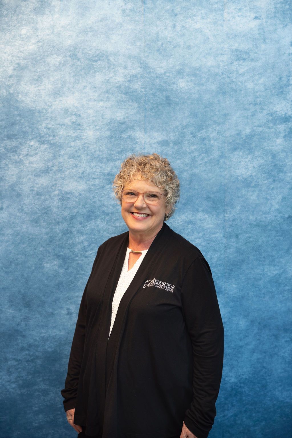 a woman wearing glasses and a white shirt is smiling for the camera .