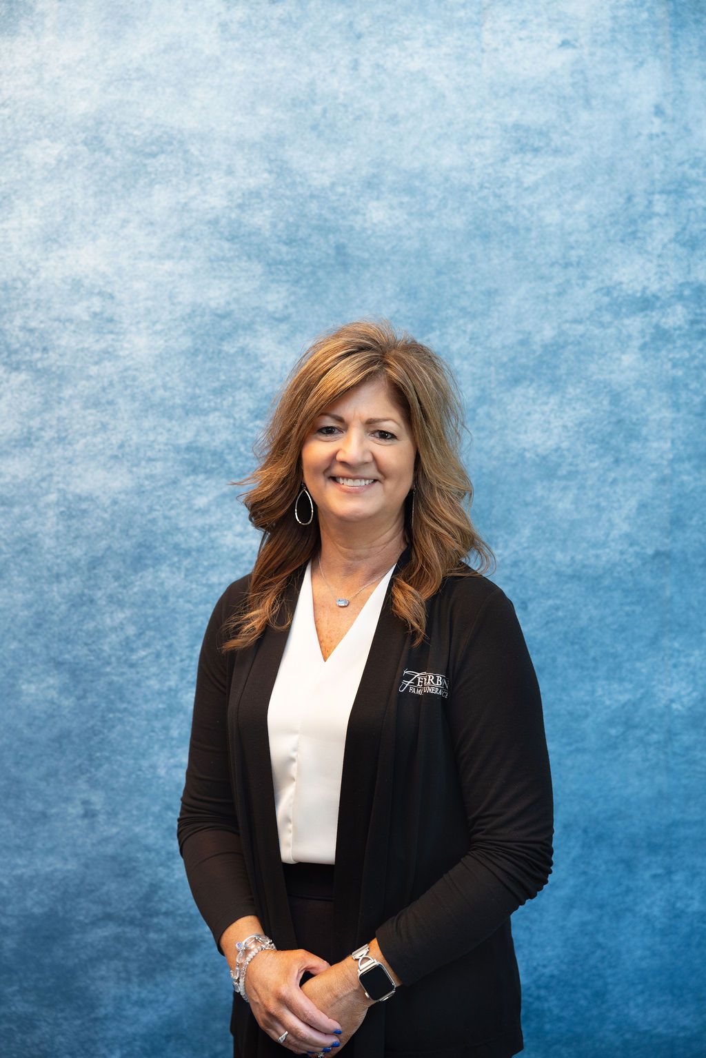a woman wearing a white jacket and earrings is smiling for the camera .