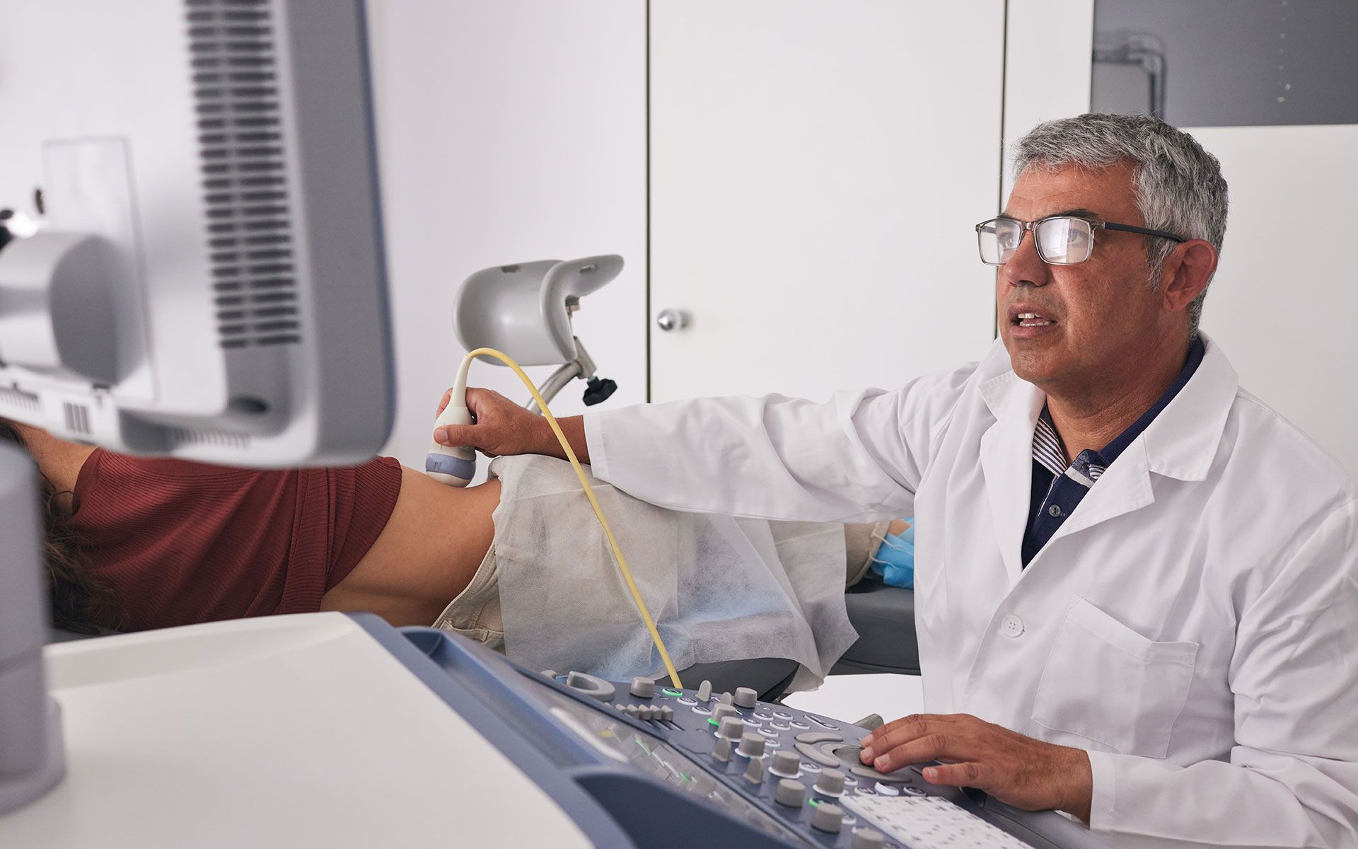 A doctor is using a computer while a patient is getting an ultrasound.