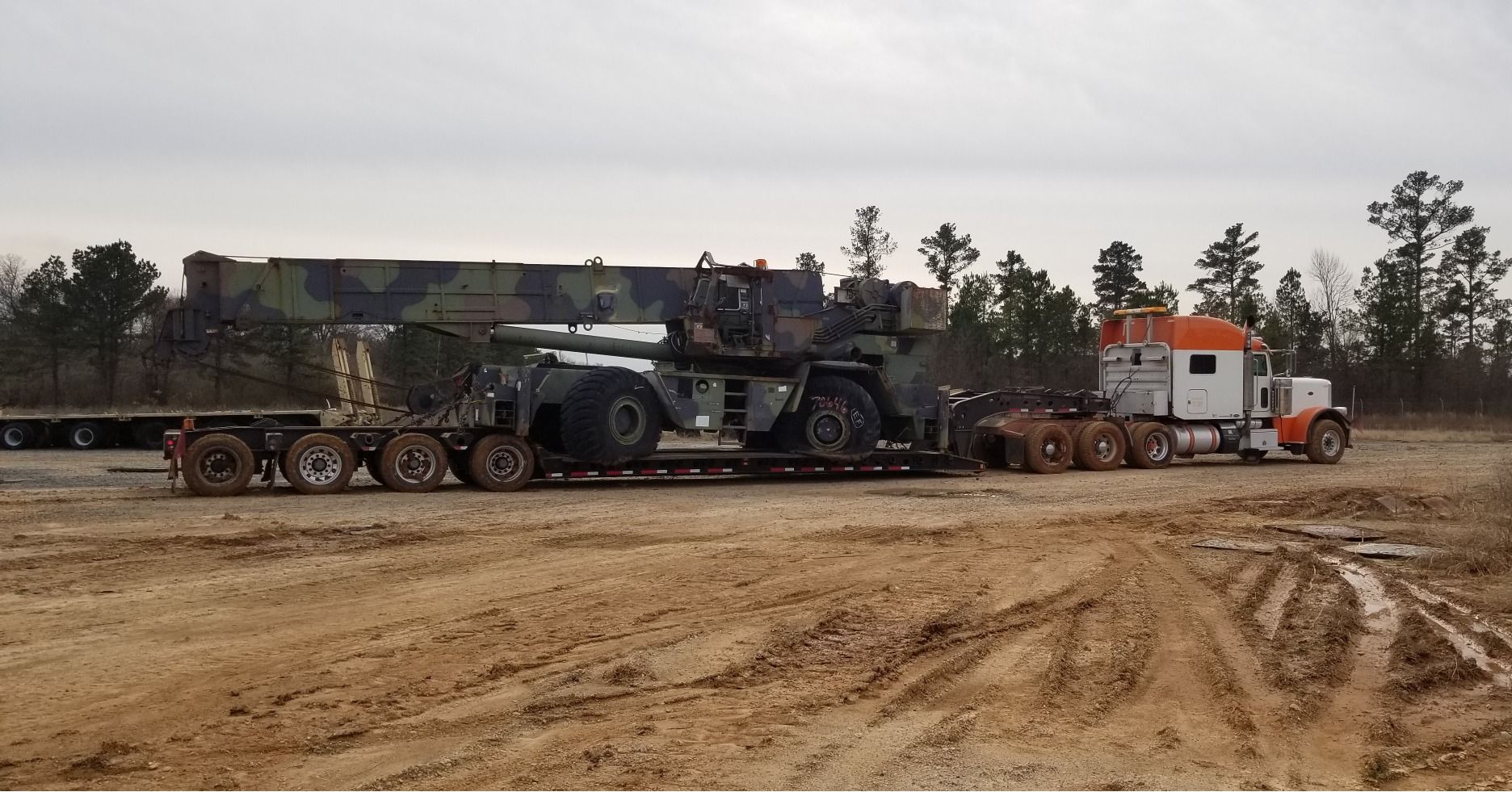 A large crane on a trailer being pulled by a truck on a dirt road.
