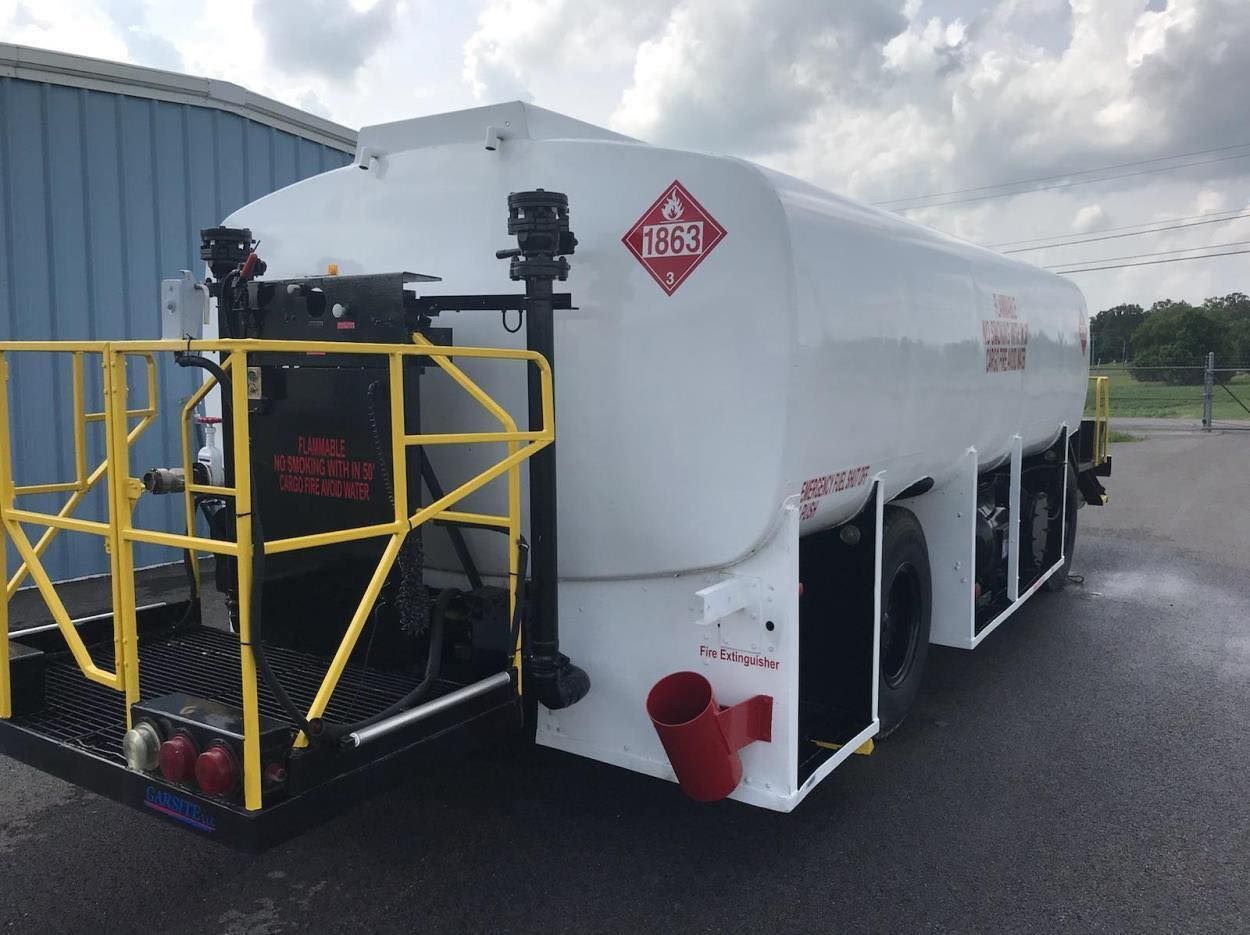White fuel tanker with yellow safety railings and a red hazardous materials diamond.