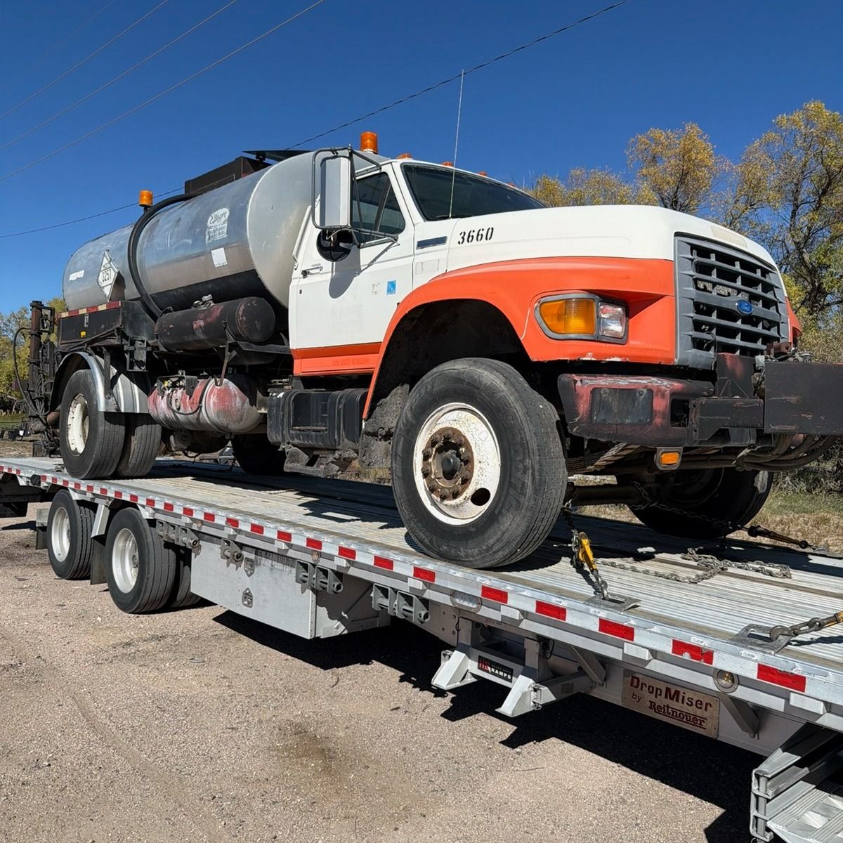 Ford tanker truck on a flatbed trailer, orange and white, parked on a sunny day.