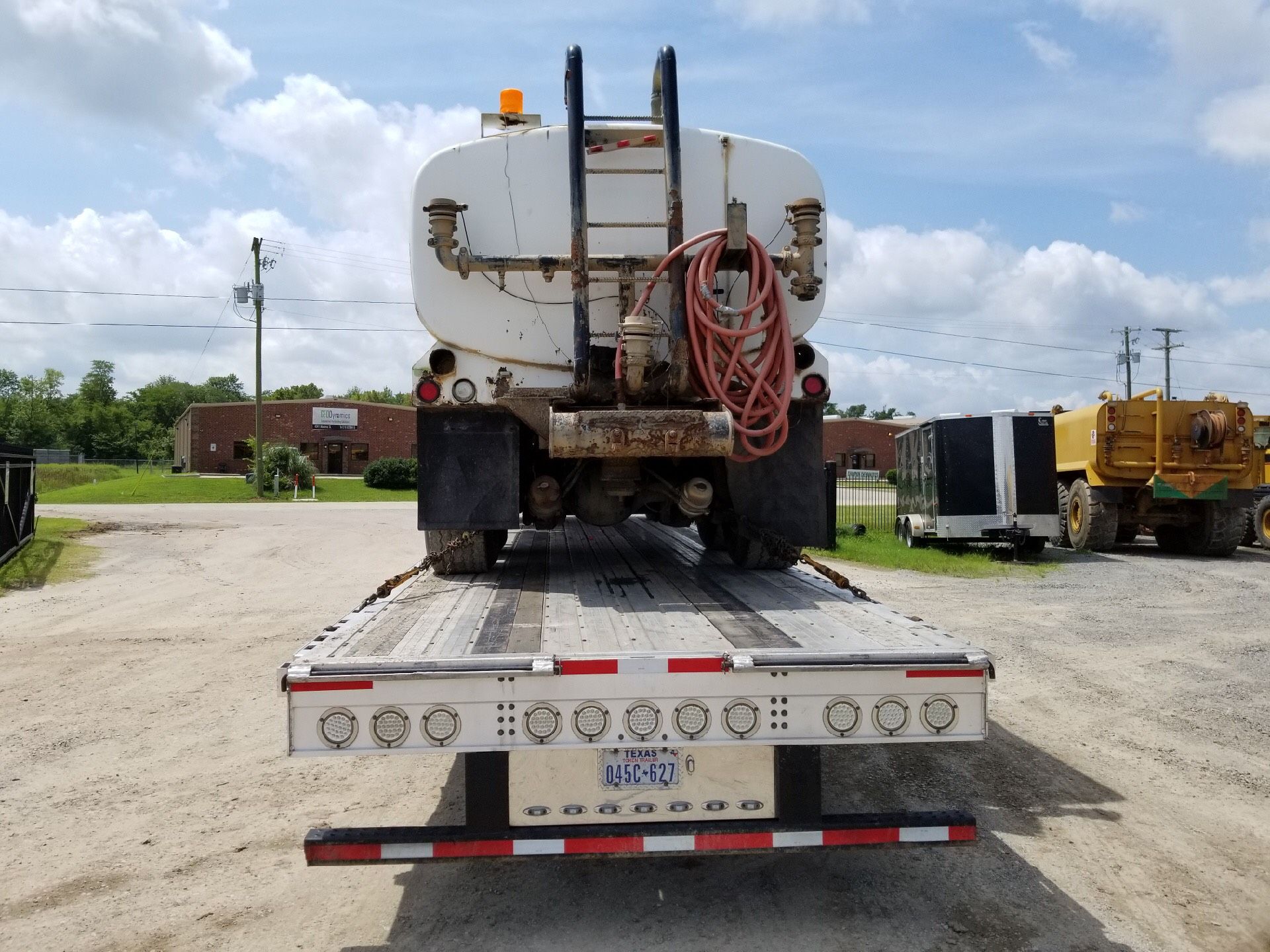 Tanker truck on a flatbed trailer, viewed from the rear, parked outdoors.