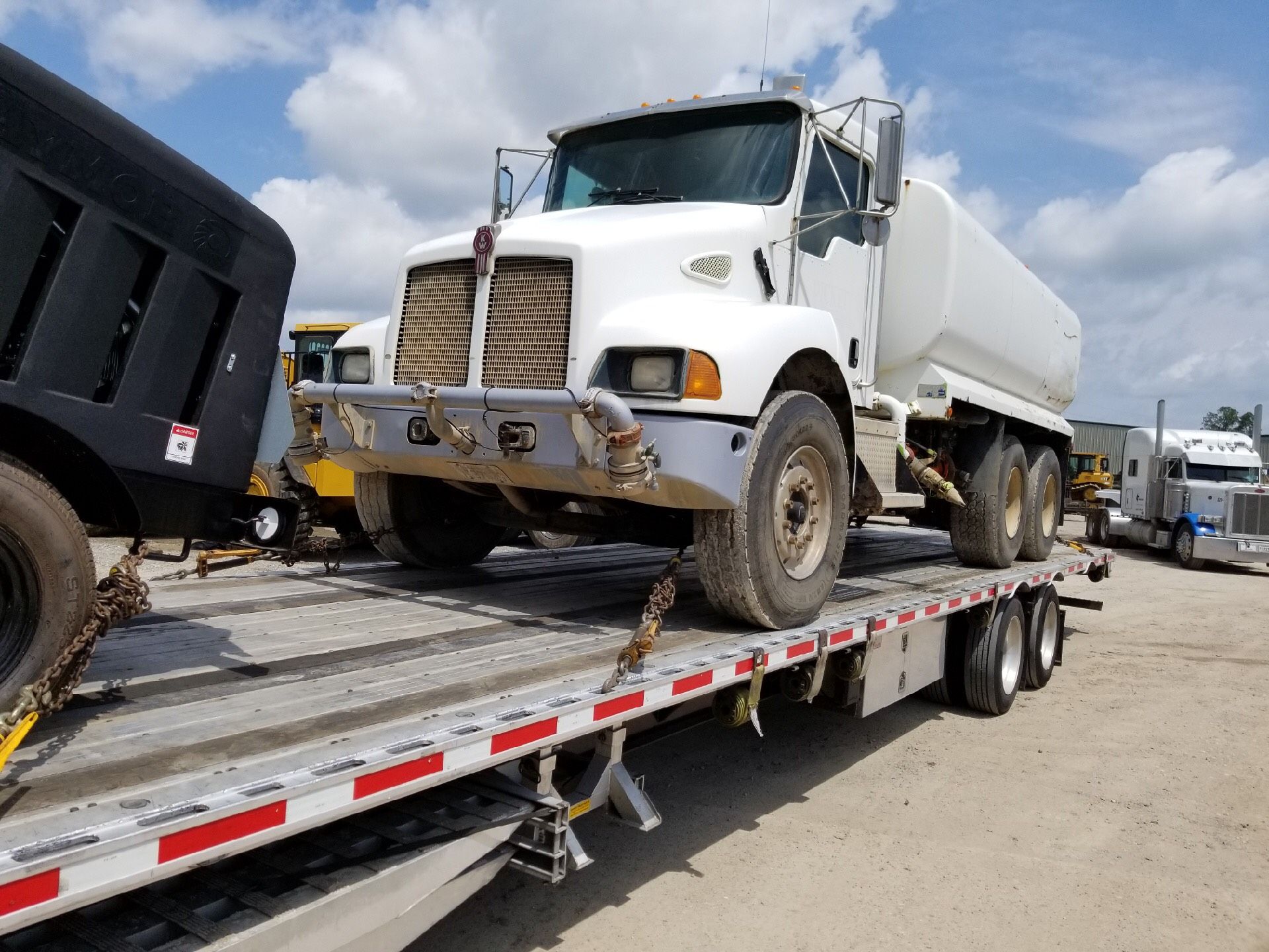 White water truck loaded on a flatbed trailer, parked on a sunny day.