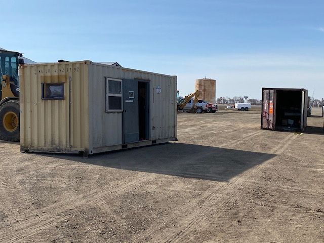 Construction site with a yellow office container, open door, and machinery on a dirt lot.