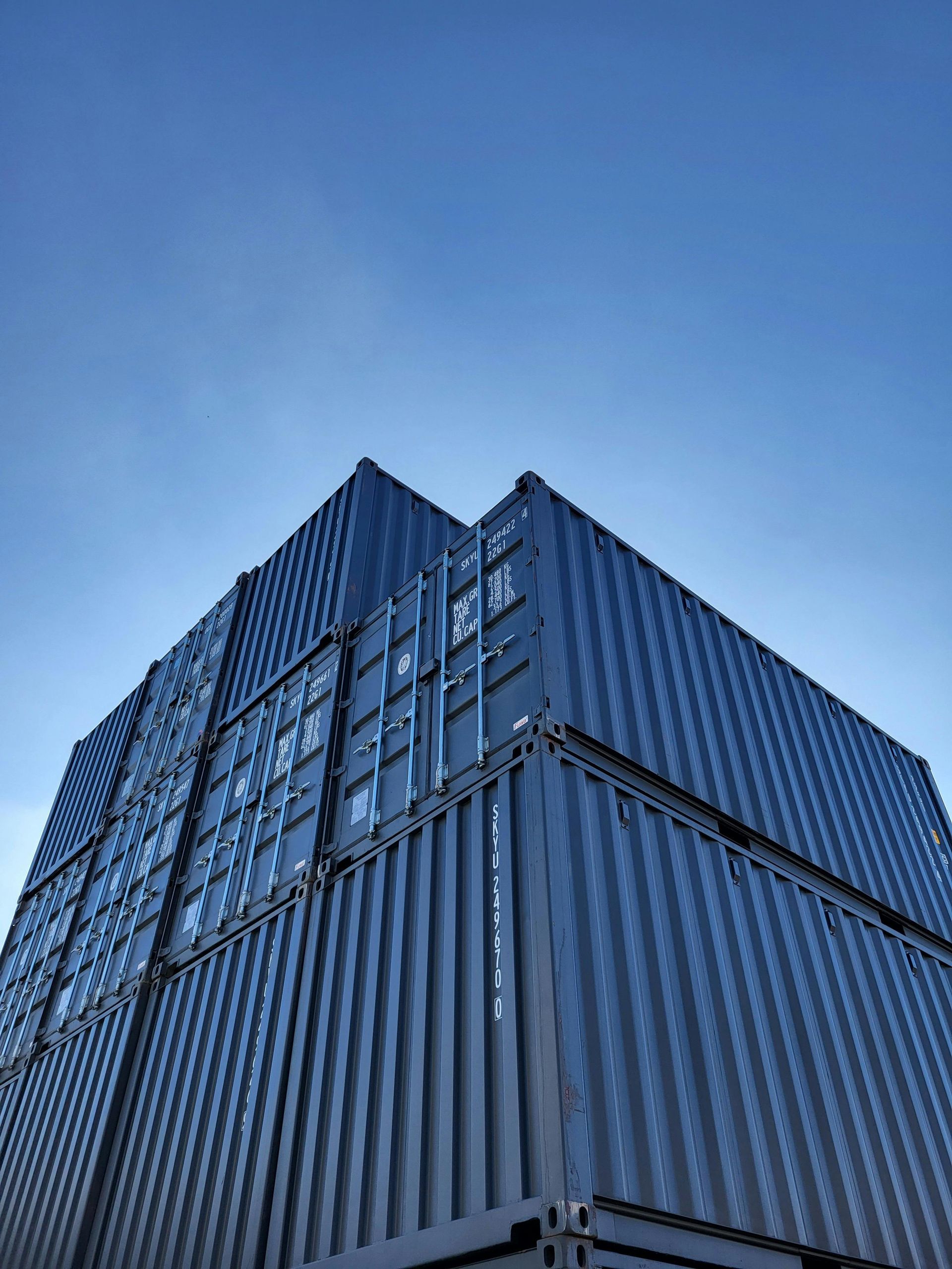 Stacked blue shipping containers against a clear blue sky.