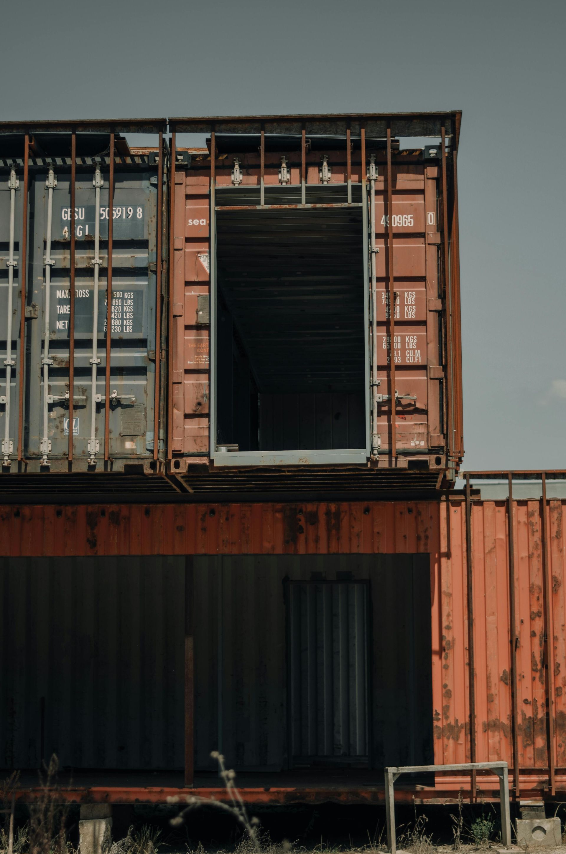 Rusty red shipping containers stacked, forming a building, with an open doorway.