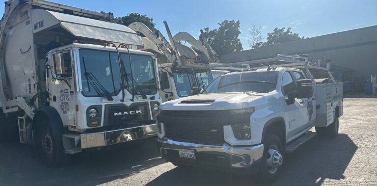 A garbage truck and a truck are parked next to each other in a parking lot.