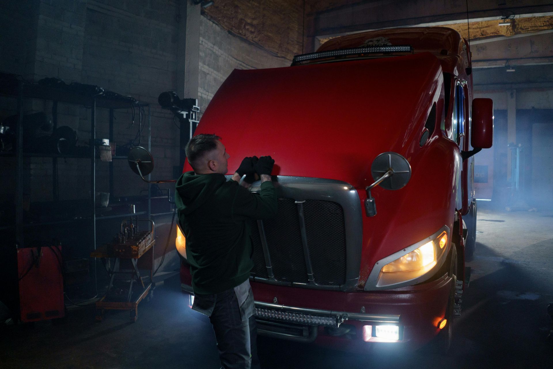 A man is working on a red semi truck in a garage.