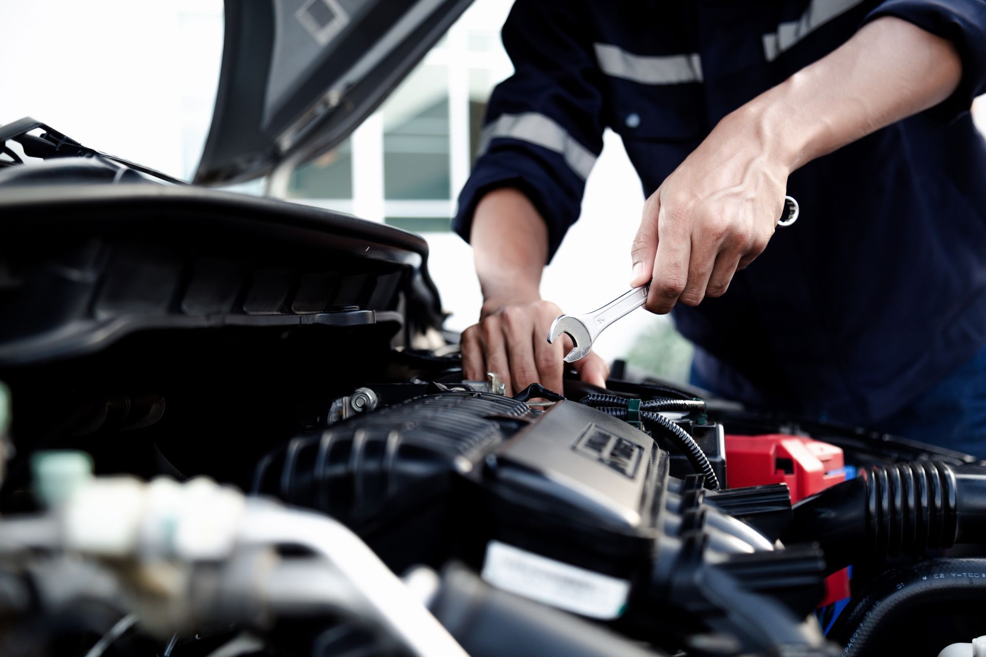 Mechanic using a wrench to work on a car engine with the hood open