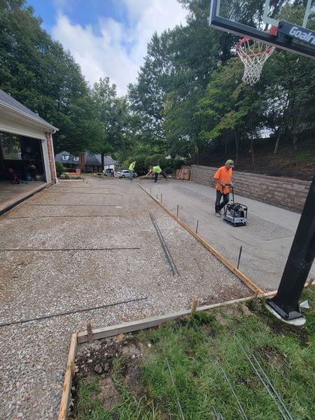 a man is working on a concrete driveway next to a basketball hoop .