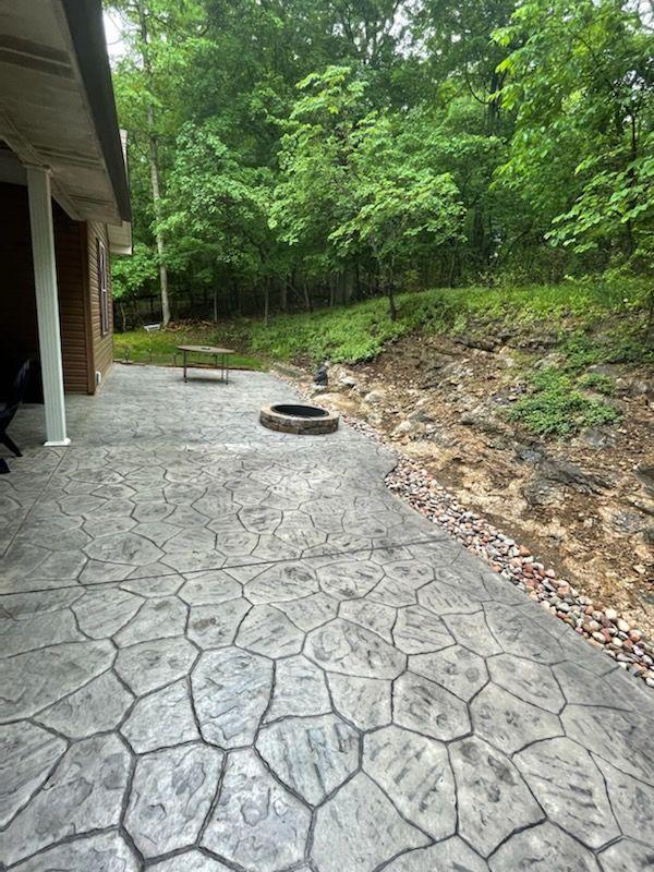 a patio with a fire pit and trees in the background .