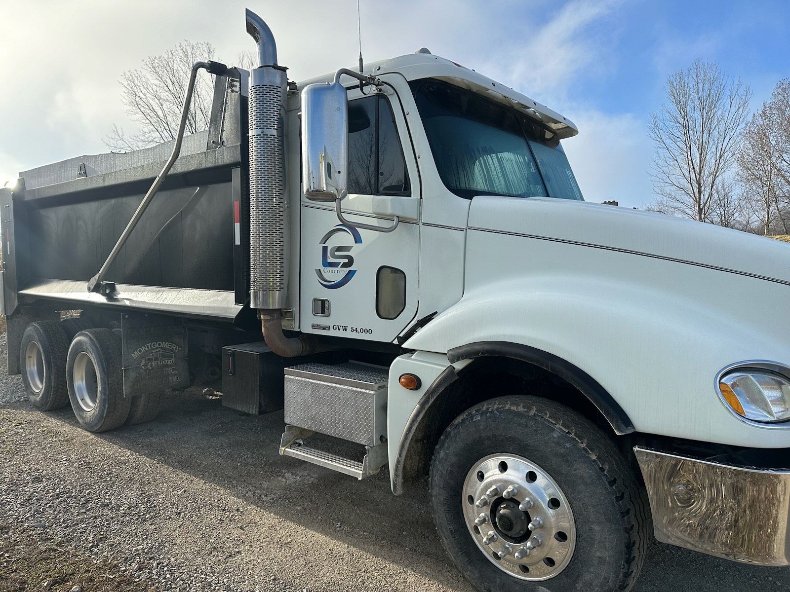 L & S Concrete STL dump truck is parked in a field on a sunny day .