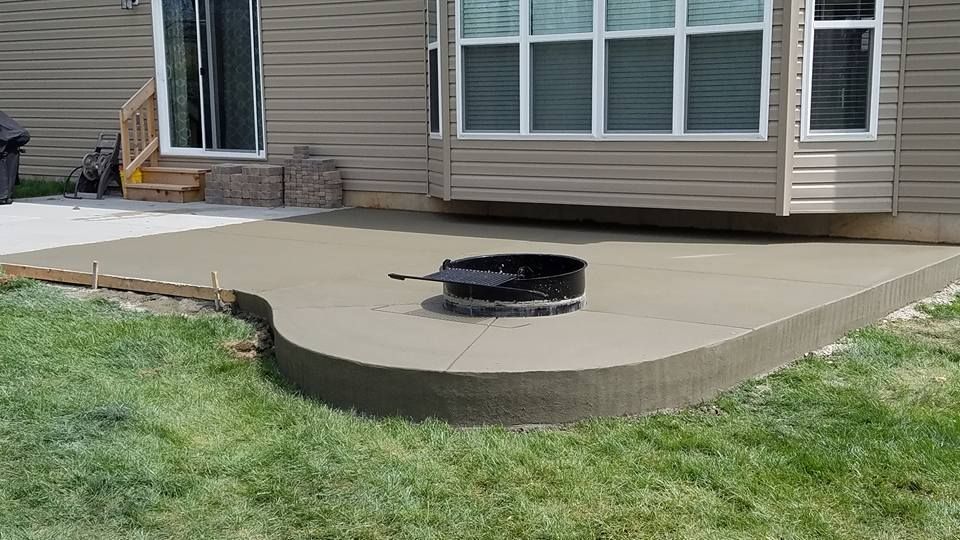 a concrete patio with a fire pit in the middle of it in front of a house .