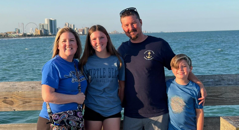 a family is posing for a picture on a pier near the ocean .