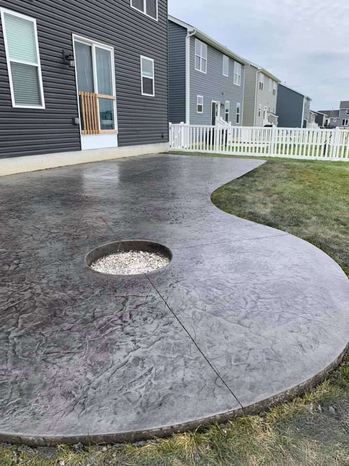a concrete patio with a fire pit in the middle of it in front of a house .