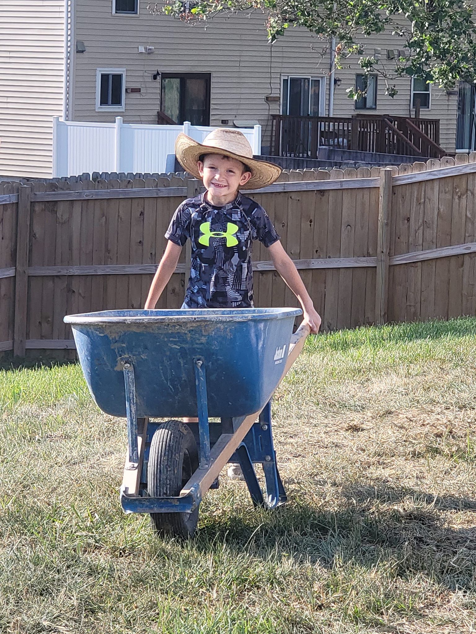 a young boy is pushing a wheelbarrow in a yard .
