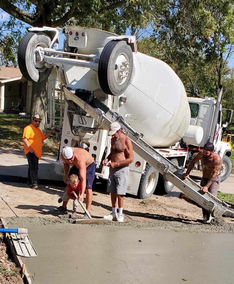 a group of men are working on a driveway next to a concrete mixer truck .