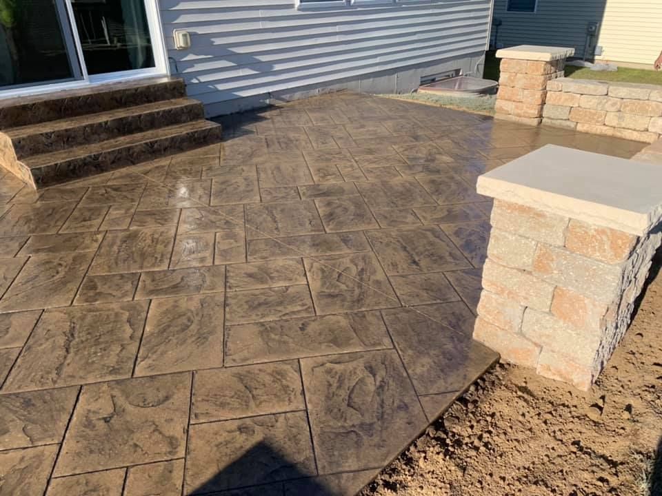 a concrete patio with stairs and a stone wall in front of a house .