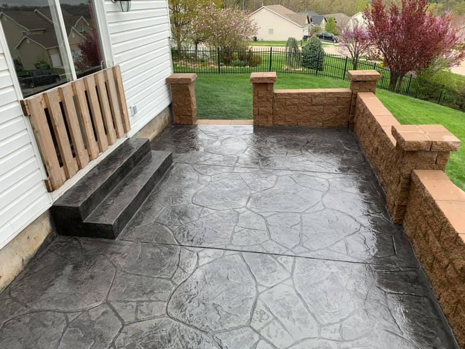 a concrete patio with steps and a brick wall next to a house .