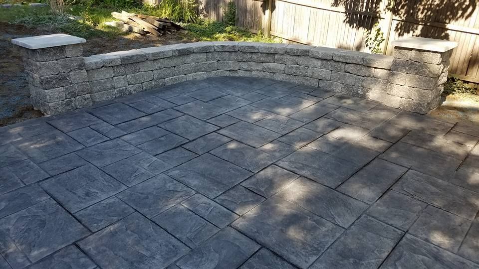 a patio with a stone wall and a bench in the backyard .
