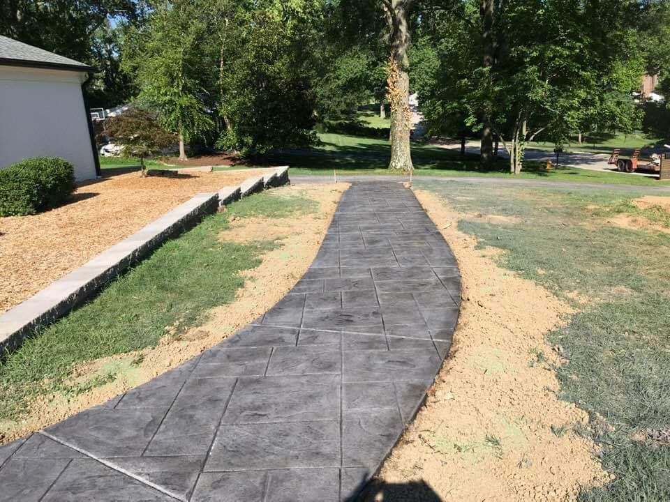 a concrete walkway leading to a house with trees in the background .