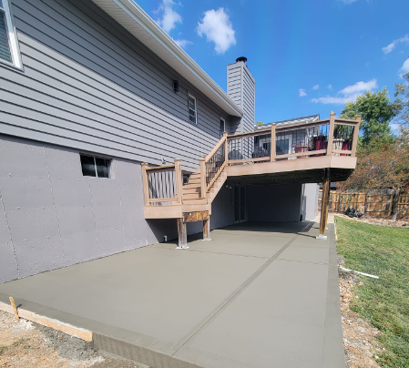 a house with a concrete deck and stairs underneath it .