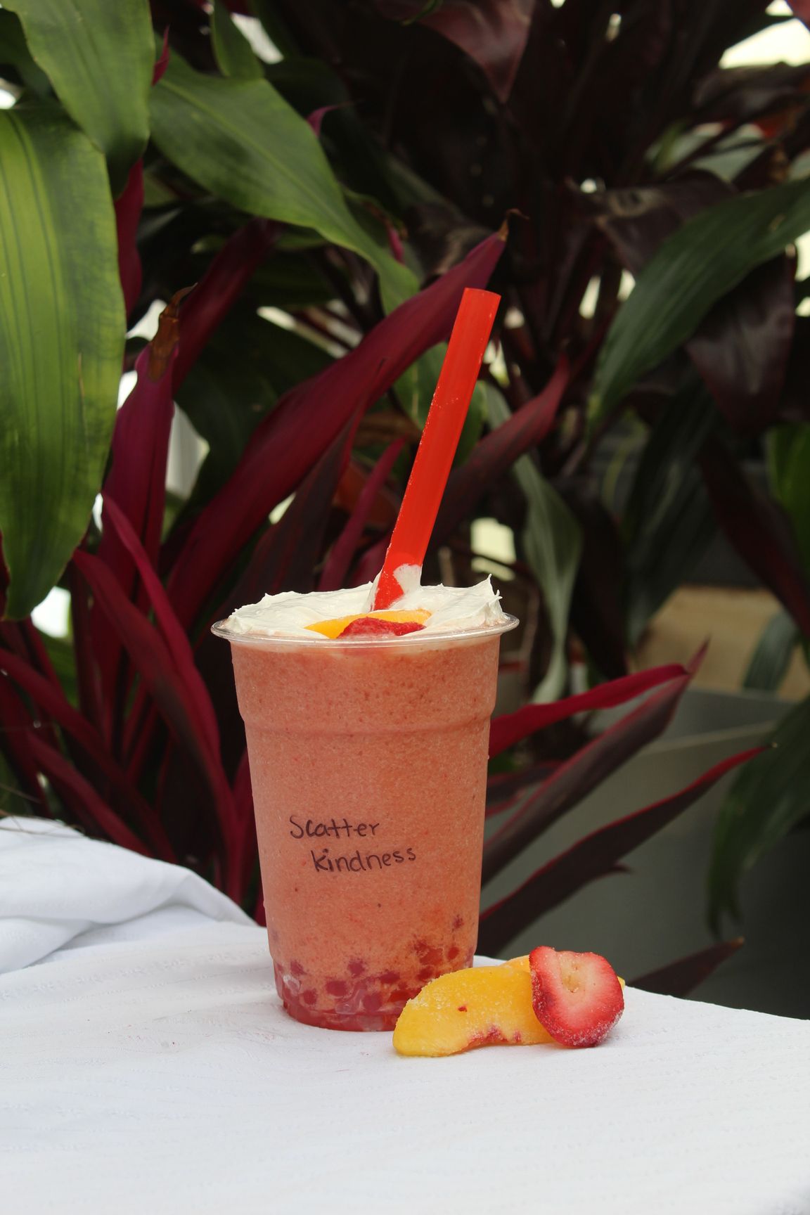 Strawberry and mango smoothie in a clear cup with whipped cream, red straw, fruit slices.