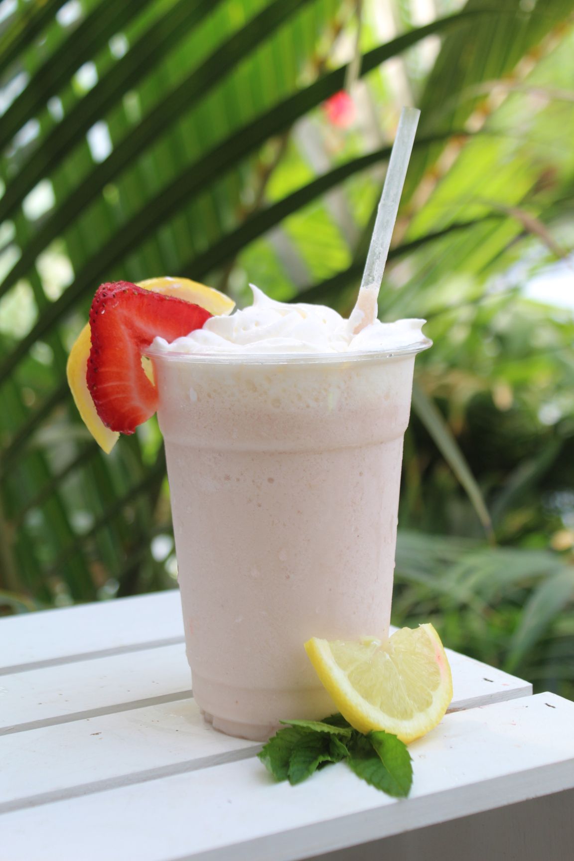 A glass of green tea with blackberries and mint leaves on a table.