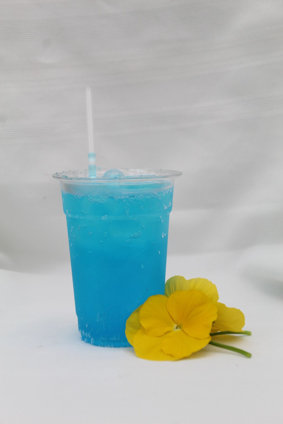 Iced coffee with whipped cream, cookie, and straw on a wooden tray against a black backdrop.