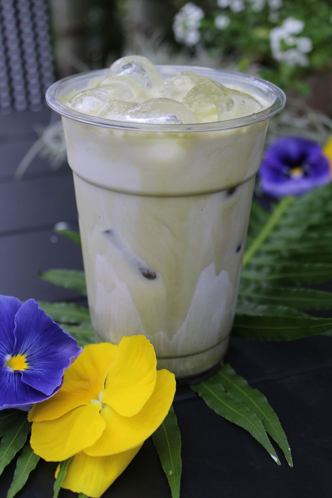 Iced coffee drink with cinnamon on top, next to pumpkins and yellow flowers on black.