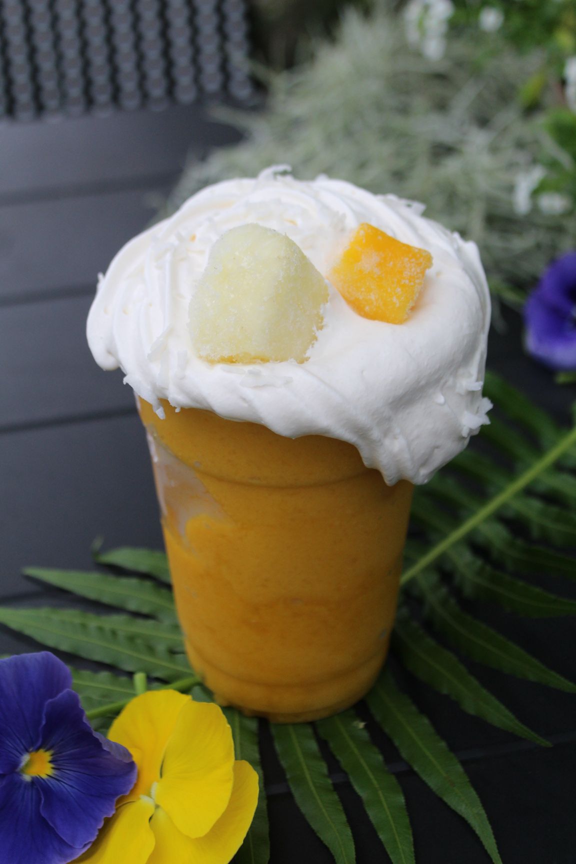 Chocolate chip cookies on a wooden serving platter, sitting on a black table with greenery in the background.