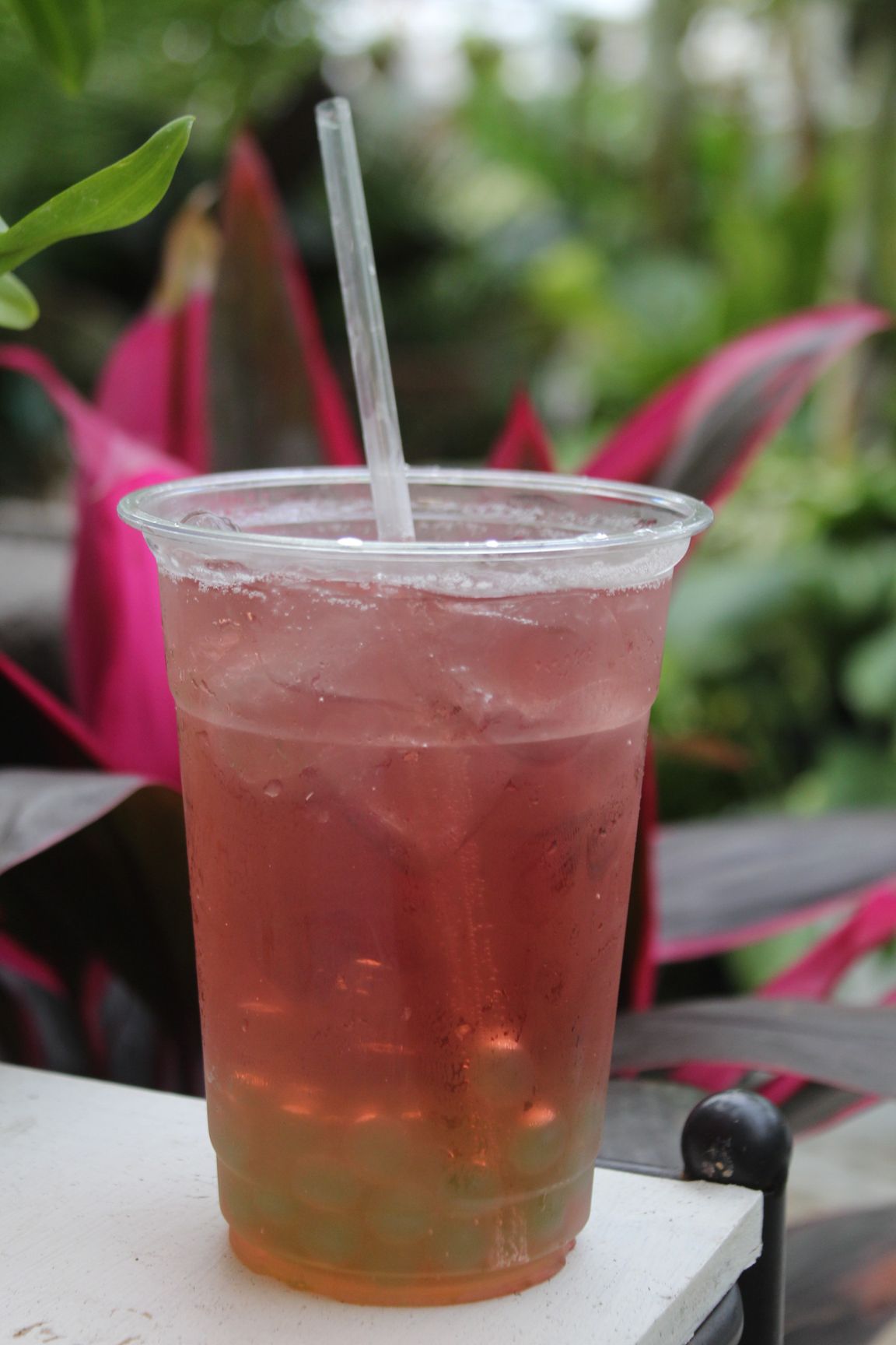 Strawberry and mango smoothie in a clear cup with whipped cream, red straw, fruit slices.