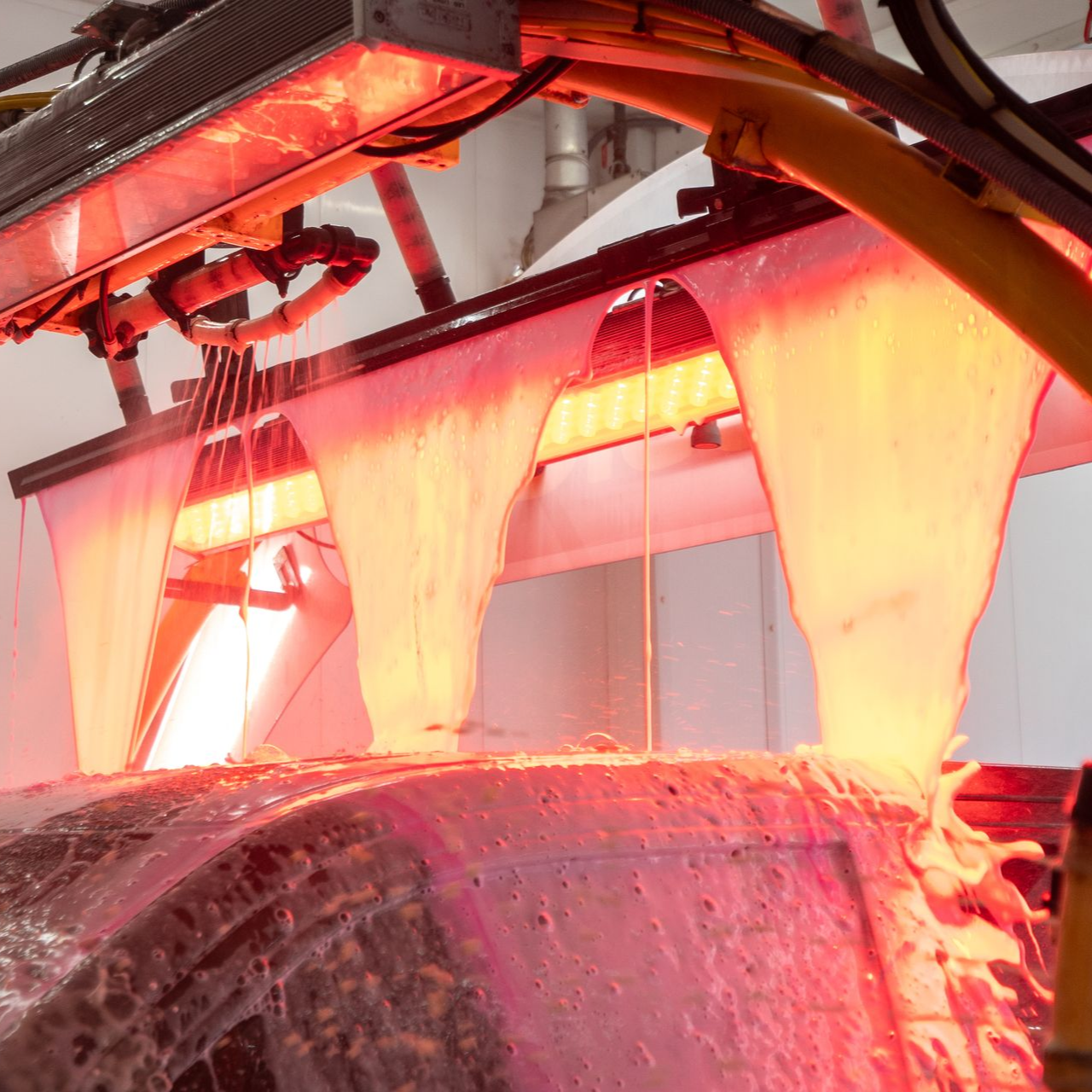 Red-lit car wash spraying a liquid over a car