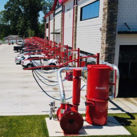 Red Eurovac vacuum system at a car wash with cars lined up for cleaning. White car wash building in background.