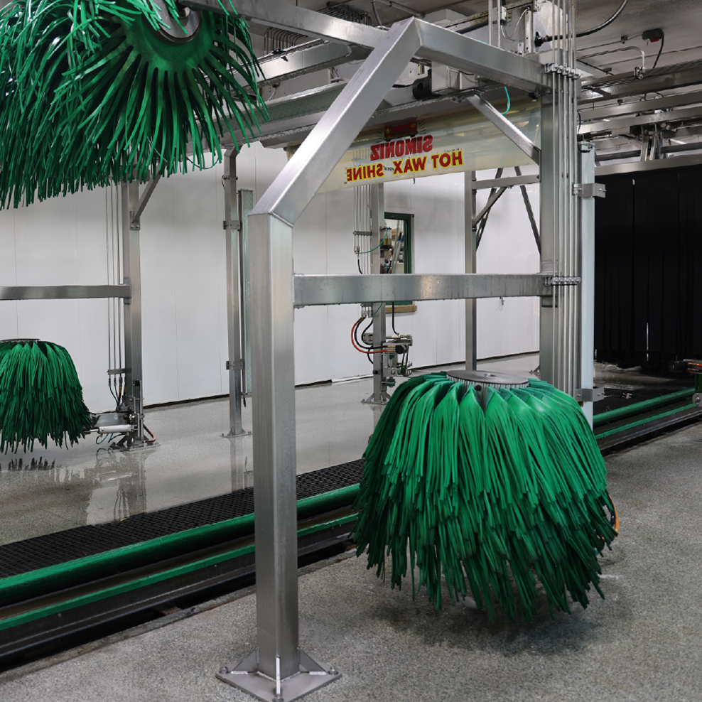 A car wash bay with green brushes, conveyor belt, and metal support beams.