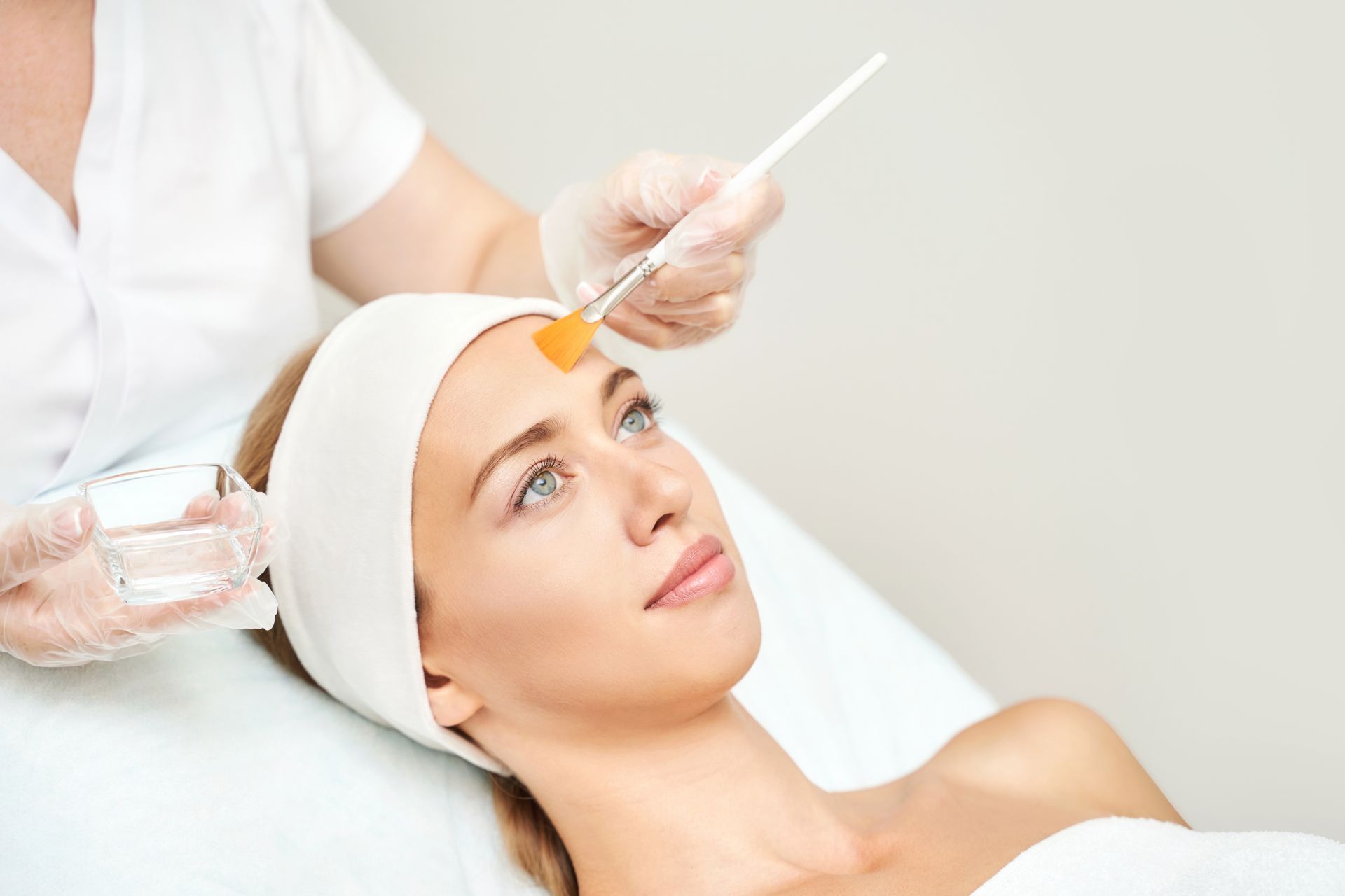 Woman receiving a facial peel treatment; a professional applies a solution to her forehead in a clinical setting.