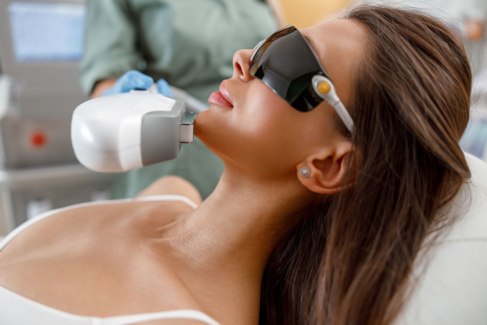 Woman receiving laser treatment on her face, wearing protective eyewear, in a clinical setting.