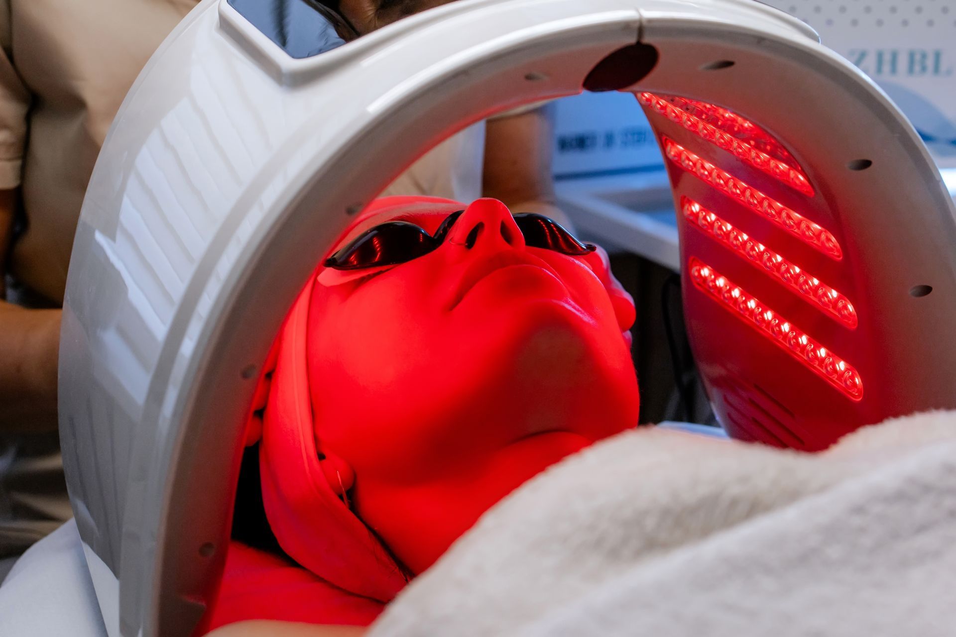 Person under red LED light therapy mask inside a treatment device