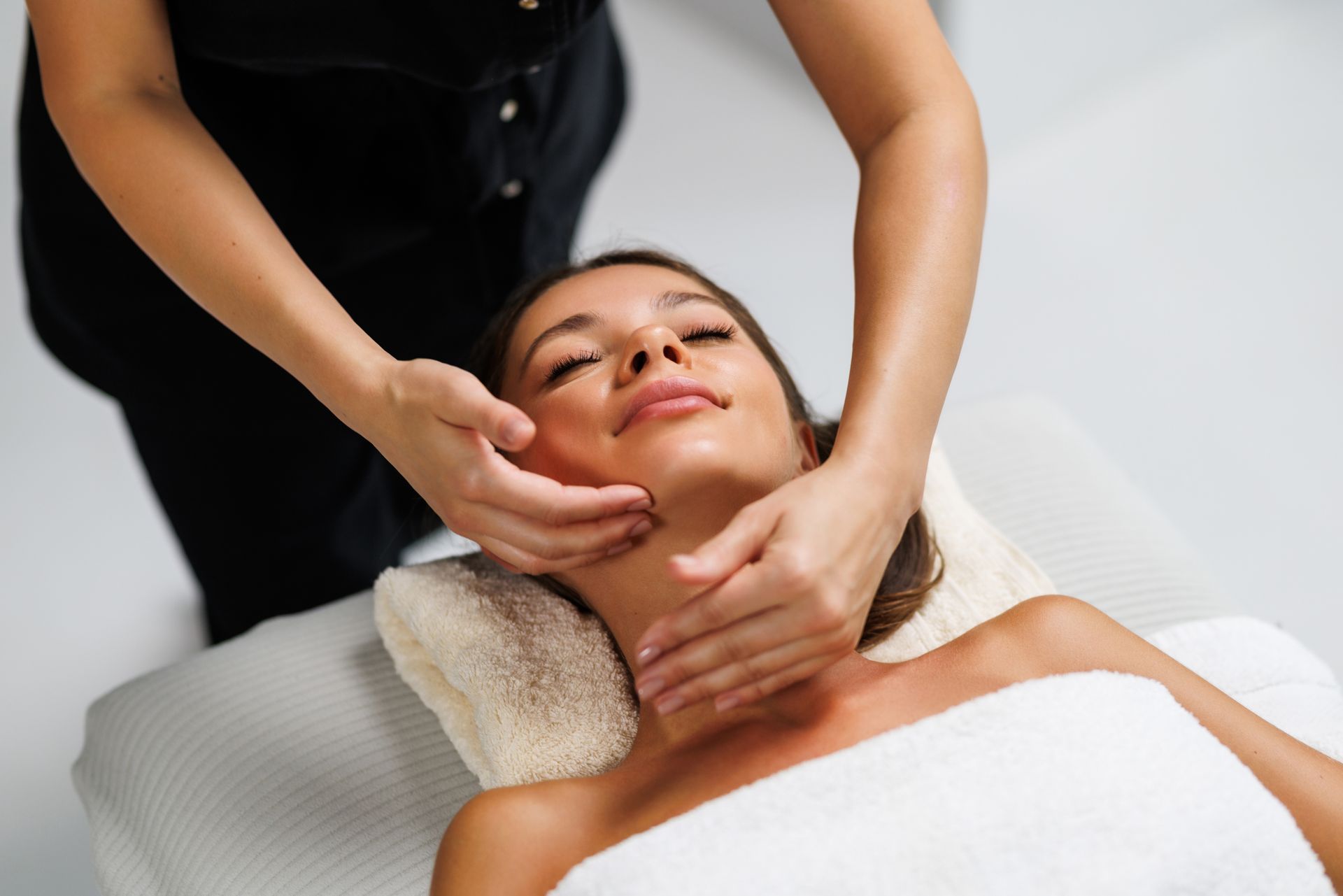 Facial massage with hands supporting the client’s chin and jaw on a spa treatment table