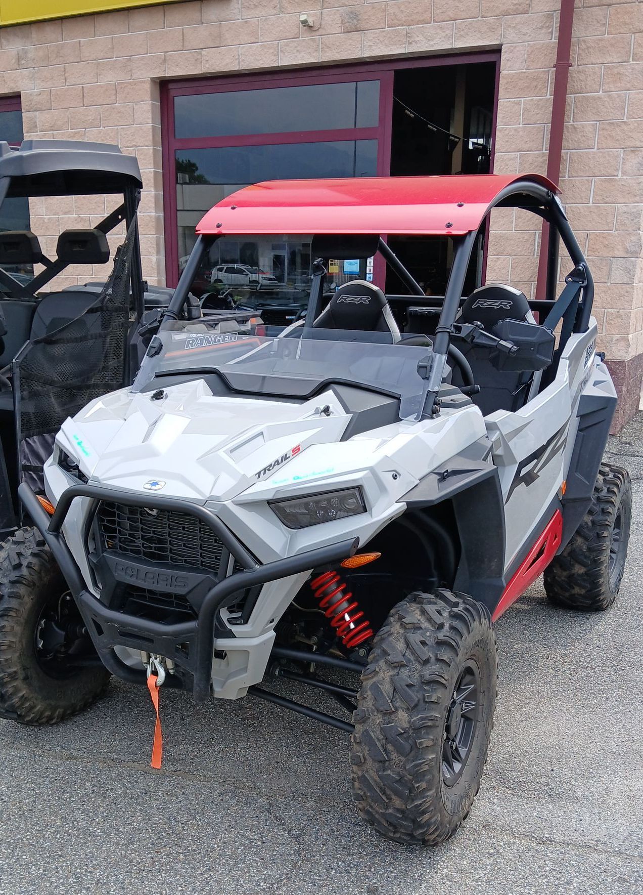 Un UTV Polaris RZR grigio e rosso affiancato, parcheggiato fuori da un edificio.
