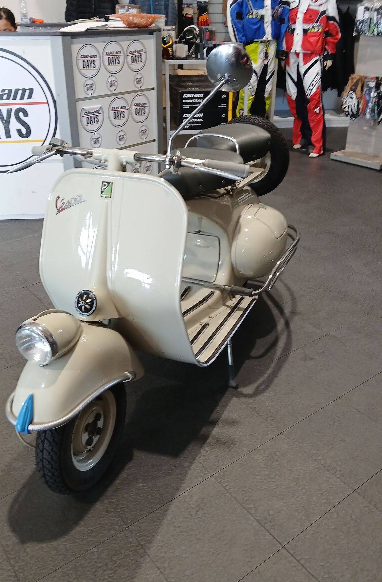 Scooter d'epoca color crema con faro anteriore e portapacchi, parcheggiato all'interno di un negozio.