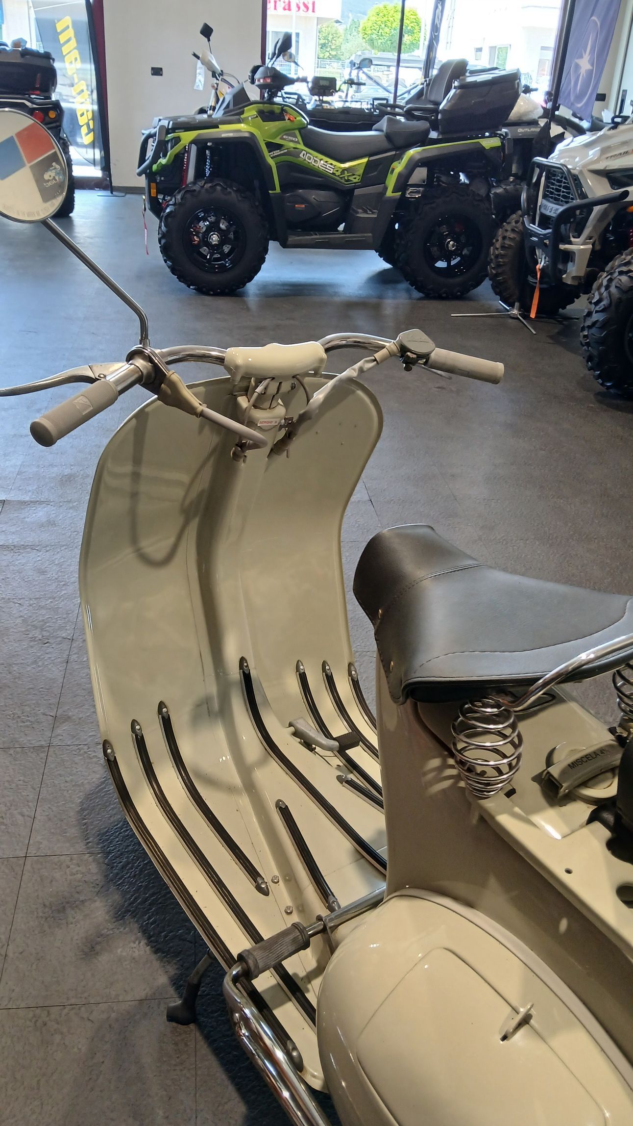 Una Vespa bianca d'epoca parcheggiata in uno showroom. Altri veicoli sullo sfondo.
