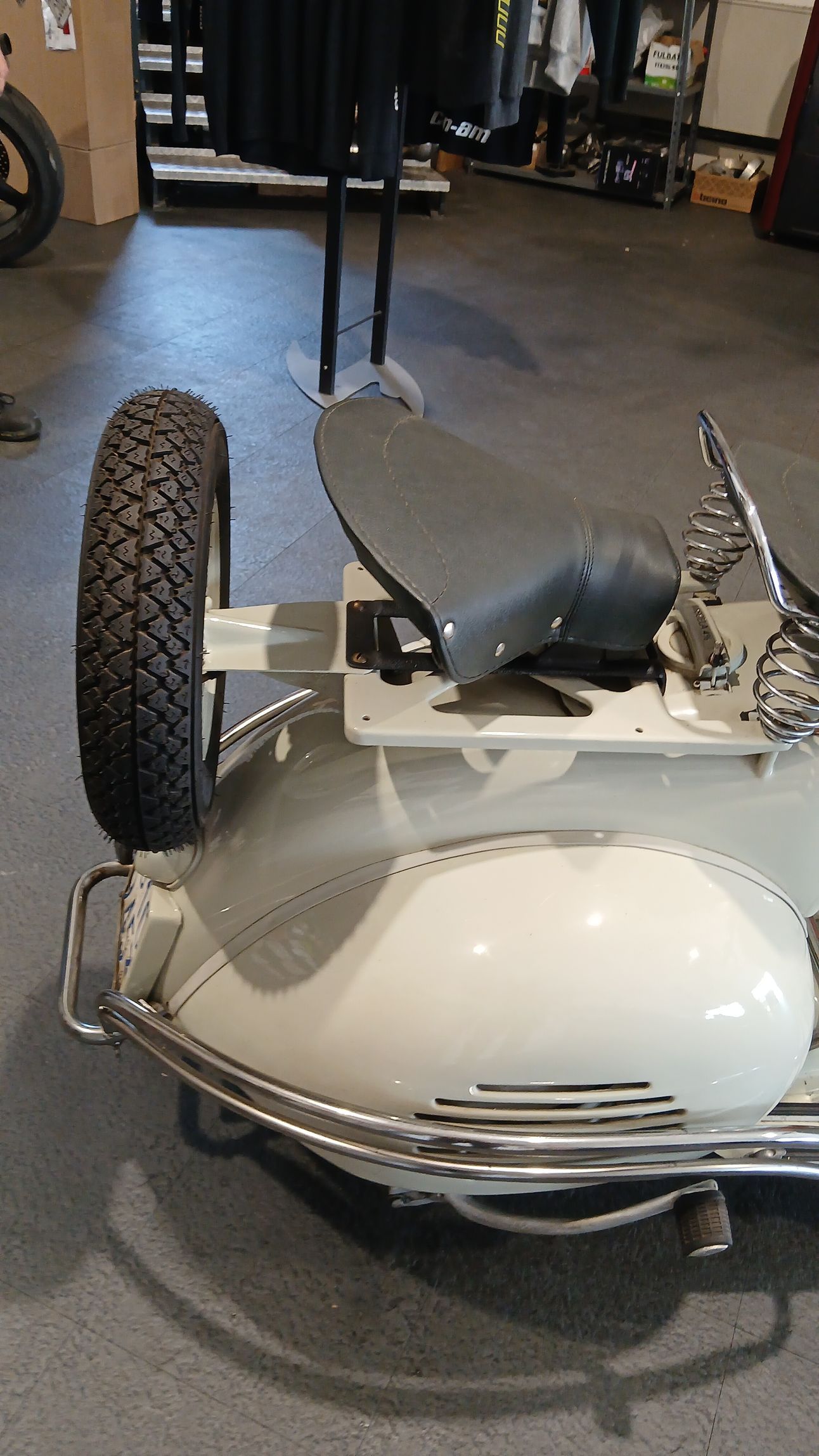 Scooter bianco d'epoca con ruota di scorta, sedile nero e dettagli cromati.