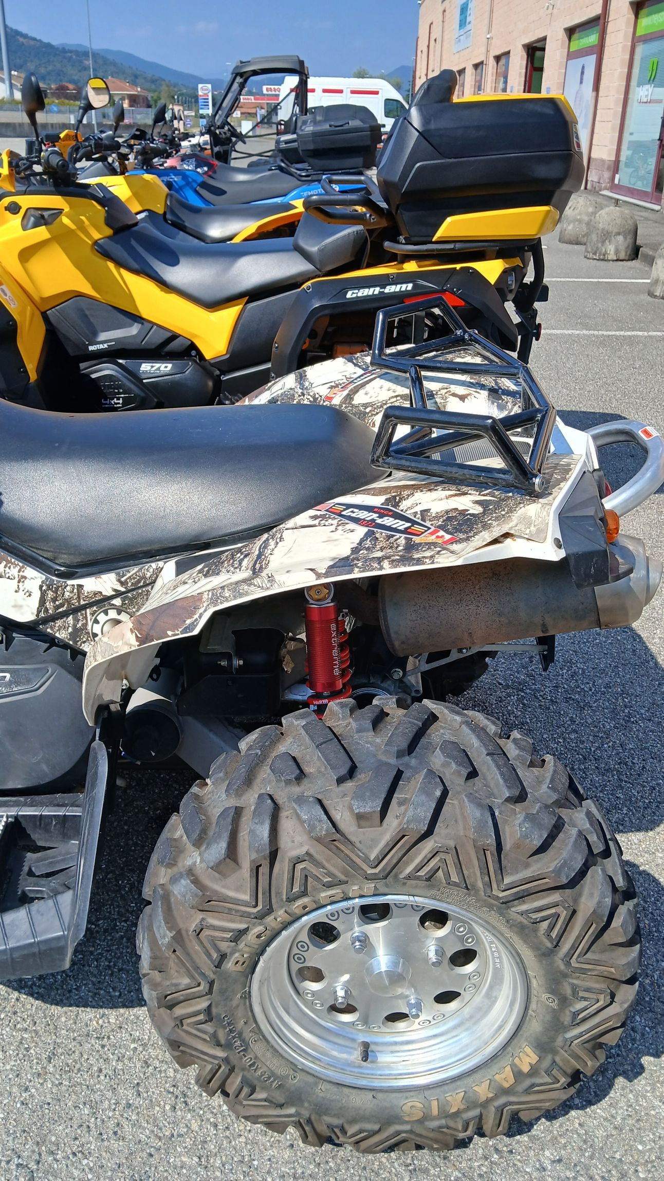 ATV con sedile mimetico e grande pneumatico fuoristrada parcheggiato all'aperto vicino a un ATV giallo.