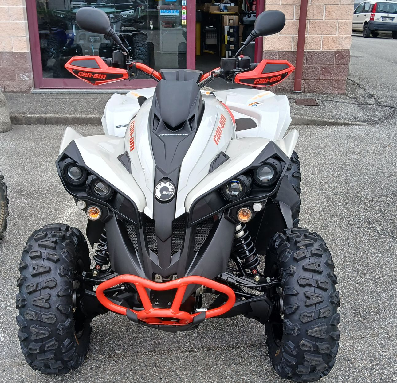 Quad bianco e nero con dettagli arancioni, parcheggiato fuori da un edificio.